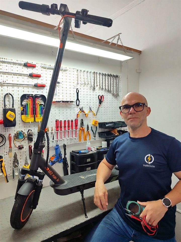 Abel Gomes, técnico da VoltCiclo, na bancada ao lado de um patinete elétrico